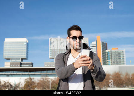 Young man with sunglasses standing against city using mobile phone Stock Photo