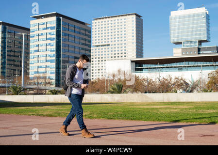 Side view of a Man using smart phone while walking against city buildings Stock Photo