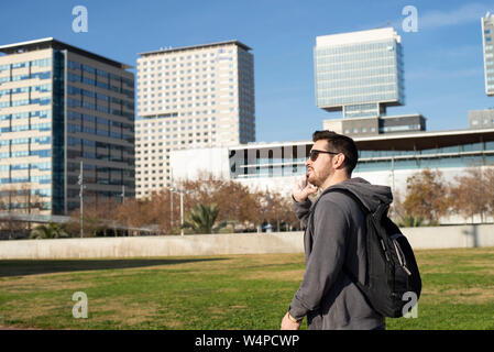 Side view of a Man using smart phone while walking against city buildings Stock Photo