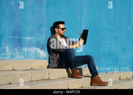 Side view of a young man with sunglasses sitting on stairs while using a tablet Stock Photo