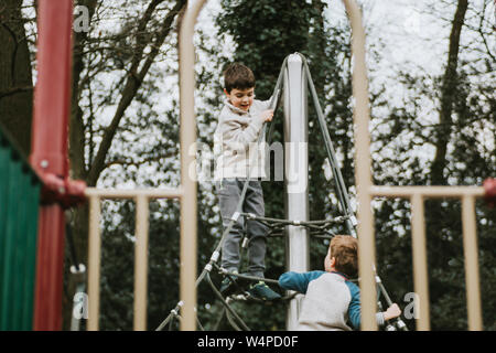 Two boys playing on climbing frame at playground Stock Photo