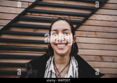 Young mixed race woman with wide smile standing on wooden wall. Stock Photo