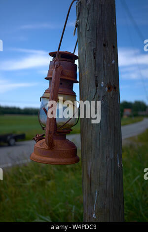 old gas kerosene lamp hanging on a wooden pole on a grass hill against the sky. Stock Photo