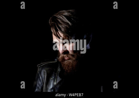 brooding bearded hipster in a leather jacket looking somewhere to the side. isolated on black background Stock Photo