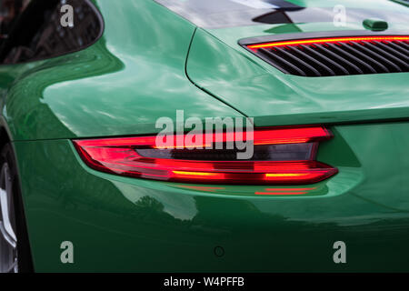 Green sports car with red backlight on. Closeup of a luxury car body. Modern LED light. Rear light strip. Stock Photo