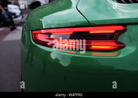 Green sports car. Car backlight on before the crosswalk. Closeup of a modern red LED light. Unexpected stop. Back of a luxury car. Stock Photo