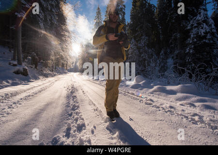 young photographer enjoying beautiful winter nature while walking on snowy country road during sunset or sunrise in forest with fresh snow Stock Photo