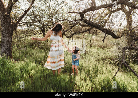 Mother and daughter holding hands and dancing in backlit meadow Stock Photo