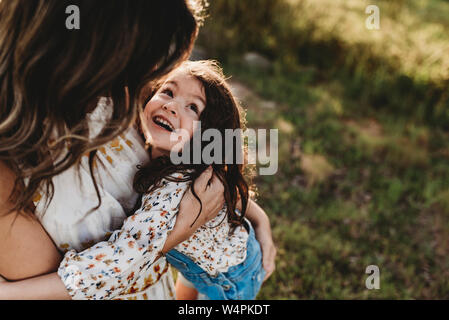 Young happy daughter laughing while being embraced by mother outside