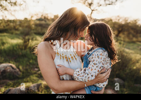 Young mother holding daughter and cuddling in bright california field Stock Photo