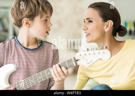 Mother and son making music together, both singing and son playing electric guitar, close-up, Germany Stock Photo