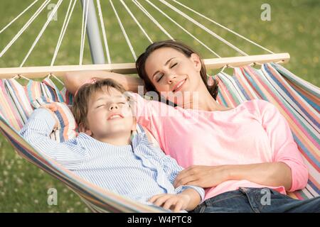 Mother and son lying in hammock, eyes closed, smiling, Germany Stock Photo