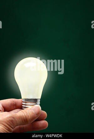 Hand holding illuminated bulb on chalkboard background with copy space . Concept of bright idea, innovation, imagination, inspiration, vision in the N Stock Photo