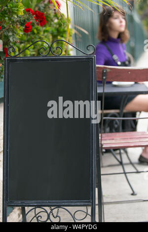 Empy blank sign board in front of a restaurant cafe or coffee shop with a female customer sitting down and waiting.  The image has copy space for logo Stock Photo