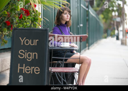 Empy blank sign board in front of a restaurant cafe or coffee shop with a female customer sitting down and waiting.  The image has copy space for logo Stock Photo