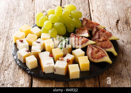 Gourmet antipasti appetizer of various cheese, fresh grapes and figs close-up on a slate board on the table. horizontal Stock Photo