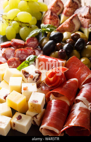 Antipasti appetizer of cheese platter, prosciutto ham, grapes, figs, sausages and olives close-up. Vertical background
