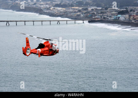 An aviation survival technician from Coast Guard Air Station San Francisco is brought aboard a MH-65 Dolphin helicopter during vertical surface training in Pacifica, California, March 19, 2019. Aircrews train regularly to ensure they are always ready to rescue those in distress. (U.S. Coast Guard photo by Petty Officer 2nd Class Jordan Akiyama) Stock Photo