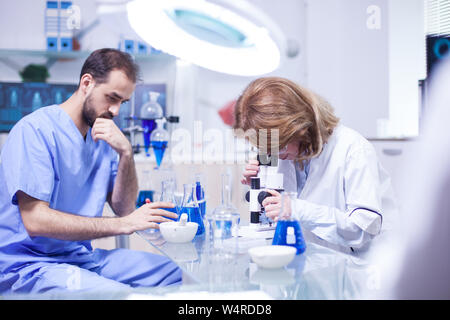 Middle age female scientist working with microscope in laboratory. Young caucasian male working as technician in a research laboratory. Stock Photo