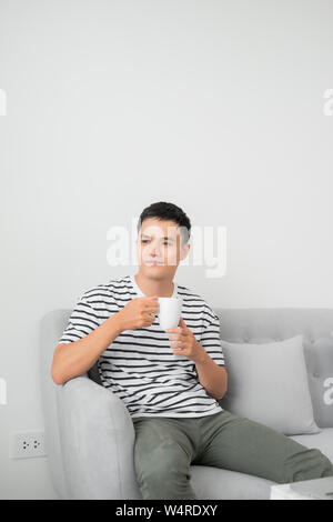 Young man concentrating on laptop computer screen, sitting at desk in living room, holding mug.? Stock Photo