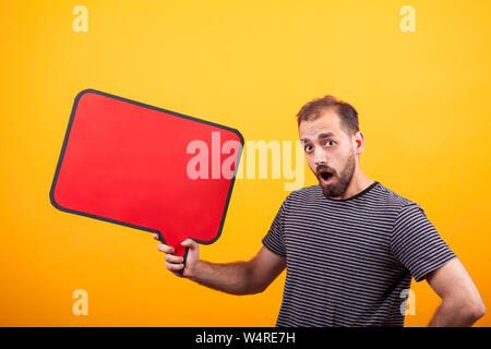 Portrait of surprised young man looking at the camera and holding a news board over yellow background. Copyspace available. Stock Photo