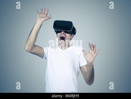 Young man using virtual reality goggles feeling excited and shock exploring virtual world making scared gestures having a scary VR adventure. Innovati Stock Photo