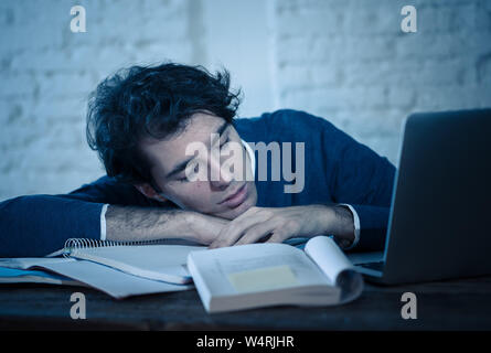 Overworked and tired male student working late at night on laptop trying not to fall asleep feeling fatigued, worried and sad. Moody dark light. Final Stock Photo