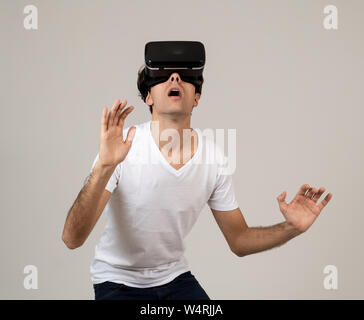 Young man using virtual reality goggles feeling excited and shock exploring virtual world making scared gestures having a scary VR adventure. Innovati Stock Photo