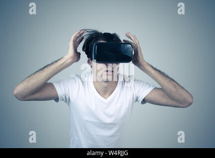 Young man using virtual reality goggles feeling excited and shock exploring virtual world making scared gestures having a scary VR adventure. Innovati Stock Photo