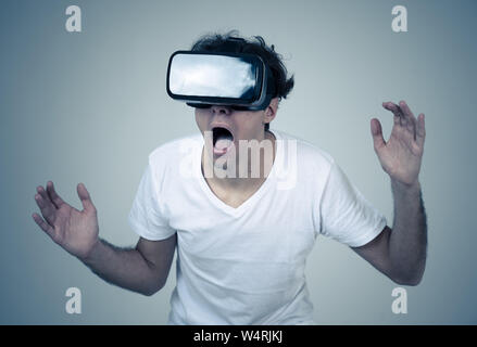 Young man using virtual reality goggles feeling excited and shock exploring virtual world making scared gestures having a scary VR adventure. Innovati Stock Photo