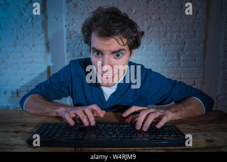 Addict young man alone at night on computer laptop feeling stressed and overwhelmed trying to finish work or winning online game or gambling. In worka Stock Photo