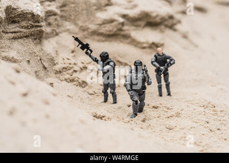 selective focus of plastic toy soldiers on sand dune with guns Stock Photo