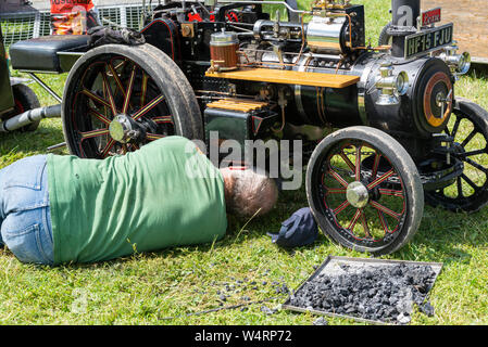 Man lying down under a steam engine to repair it at a summer fete, England, UK Stock Photo