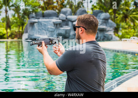 A sympathetic man launches a drone for flight, with which you can take photos and videos, near the swimming pool, view back. Stock Photo