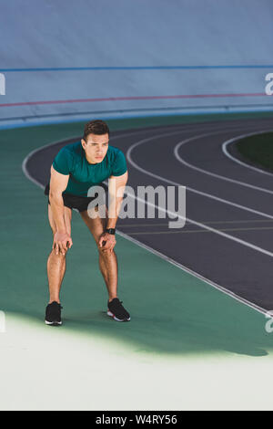 mixed race sportsman with hands on knees standing at stadium Stock Photo