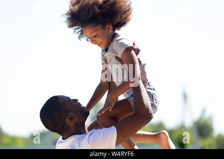 Happy african dad lifting daughter up having fun together outdoors Stock Photo