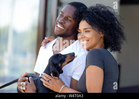 Happy african millennial couple standing outdoors holding dachshund puppy Stock Photo