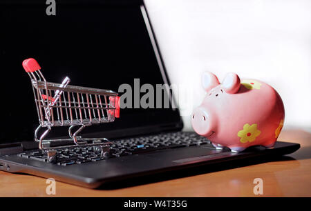 Saving money with online shopping: Laptop with a small trolley and a piggy bank on top of it Stock Photo