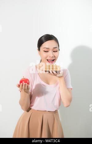 Woman holds in hand cake sweet and apple fruit choosing, trying to resist temptation, make the right dietary choice. Weight loss diet dilemma gluttony Stock Photo
