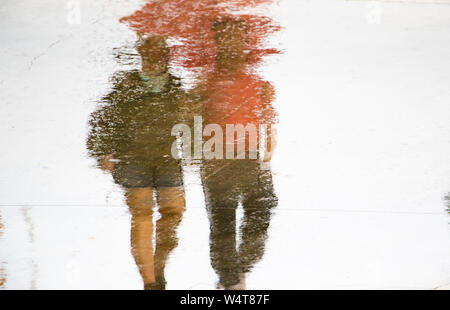 Blurry reflection silhouette in a puddle of couple holding hands while walking on a rainy summer day Stock Photo