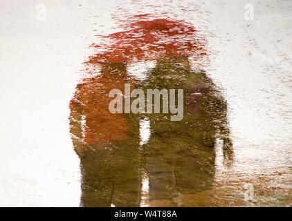 Blurry reflection silhouette  in a puddle of couple holding hands while walking on a rainy summer day Stock Photo