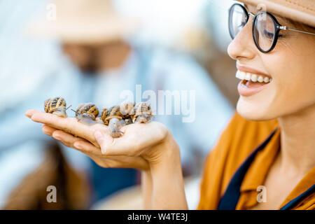 Close-up portrait of a young woman holding snails, taking care of them in the farm for snails growing Stock Photo