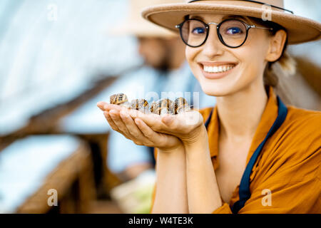 Close-up portrait of a young woman holding snails, taking care of them in the farm for snails growing Stock Photo