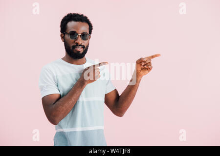 handsome african american of man in sunglasses pointing aside, isolated on pink Stock Photo
