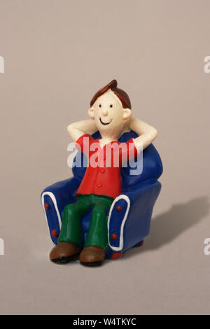 Plastic model caricature of a young man relaxing in an armchair against a plain background. Stock Photo