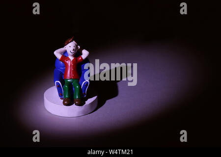 Plastic model caricature of a young man relaxing in an armchair on a plain podium and highlighted in a spotlight. Stock Photo