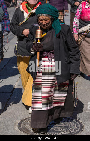 China, Tibet, Lhasa, An older Tibetan woman pilgrim circumambulates the Jokhang Temple with her mala rosary beads also wearing her traditional colorful pangden or bangdian apron. Stock Photo