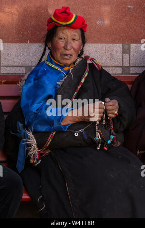 China, Tibet, Lhasa, A Tibetan woman in her heavy chuba or chupa sheepskin-lined coat holds her mala rosary beads while on a pilgrimage. Stock Photo