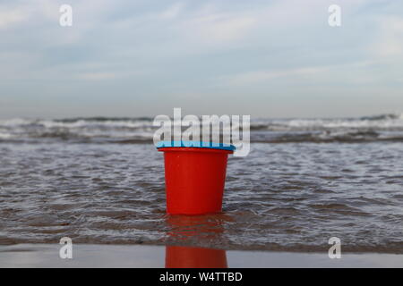 red children's play bucket in the water at the beach, Westkapelle, Netherlands Stock Photo