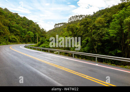 New asphalt road with bike path, forest next to it, blue sky with clouds Stock Photo